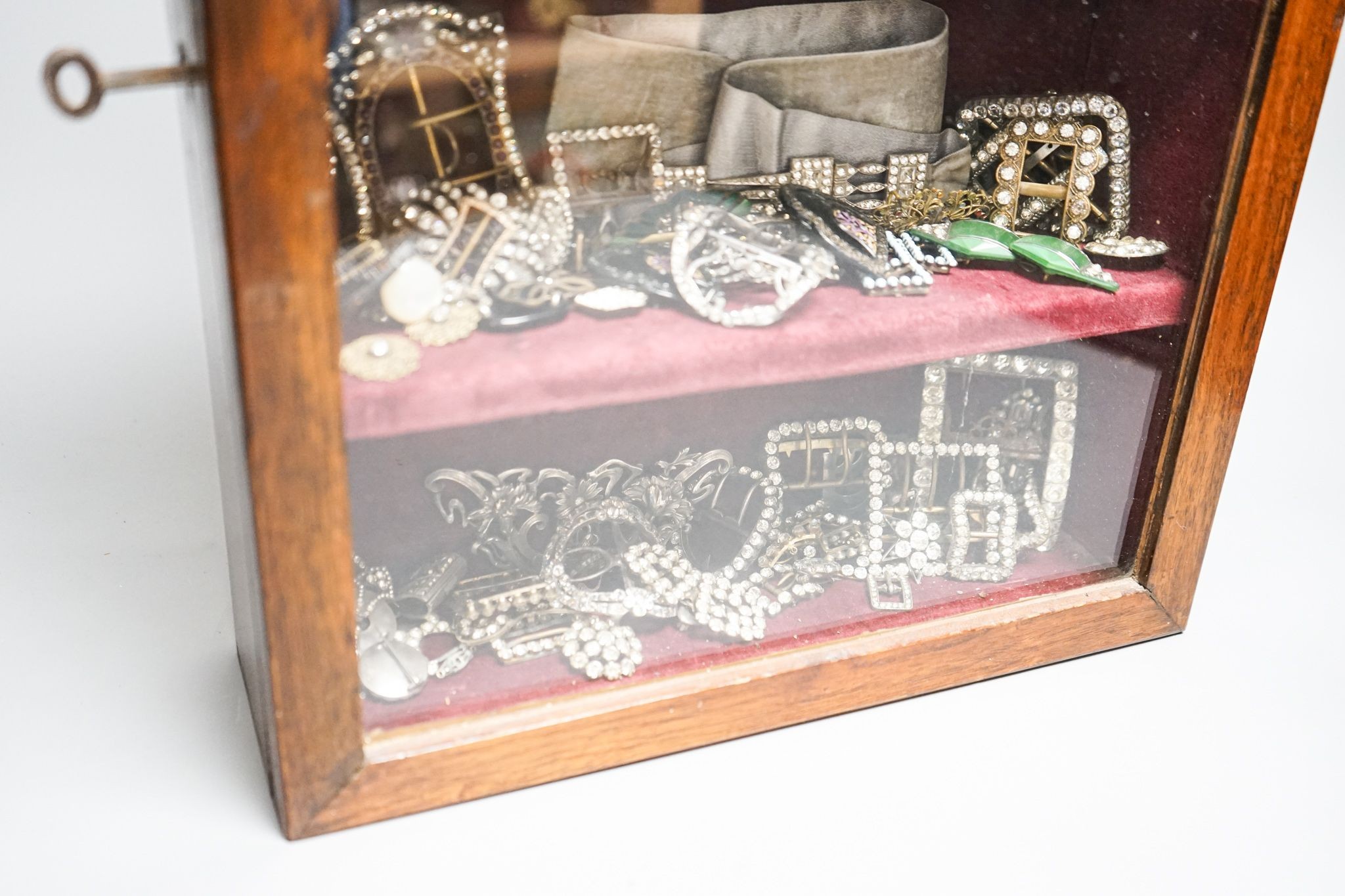A large collection of 19th/20th century paste and enamel belt and shoe buckles and clips, contained in an oak display cabinet. 56cm